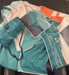  La serviette de plage qui fait 90 x 170 cm est ici en arrière plan. Le petit carré représente la débarbouillette et, sur la droite se trouve le linge à vaisselle. À noter que le petit étui d’environ 25 cm de longueur destiné à accueillir la serviette pour la transporter ou la ranger. - Magazine Camper